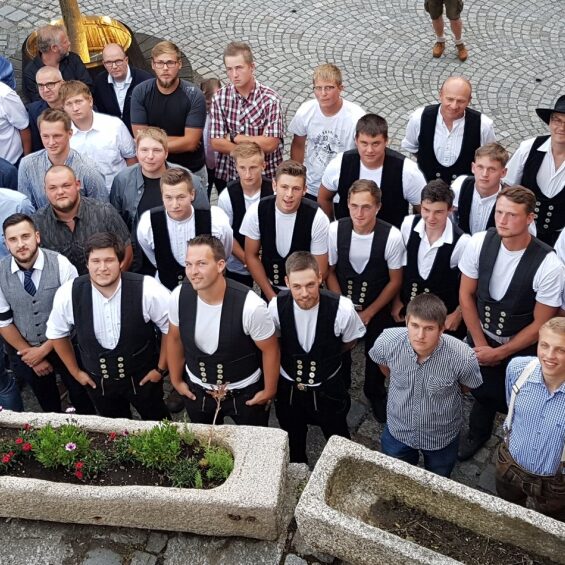 Große Gruppe junger Handwerker in traditioneller Zimmermannskleidung und zivil gekleideten Personen, Aufnahme von oben.