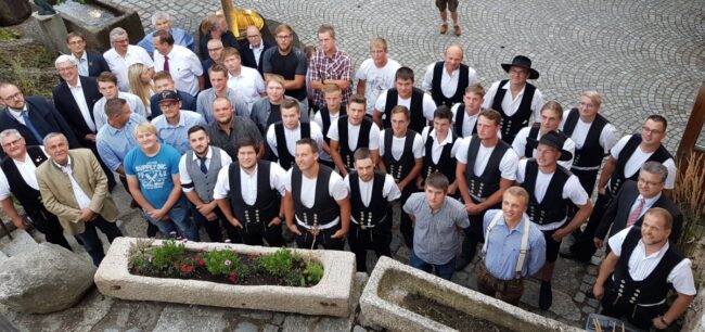 Freisprechungsfeier Große Gruppe junger Handwerker in traditioneller Zimmermannskleidung und zivil gekleideten Personen, Aufnahme von oben.