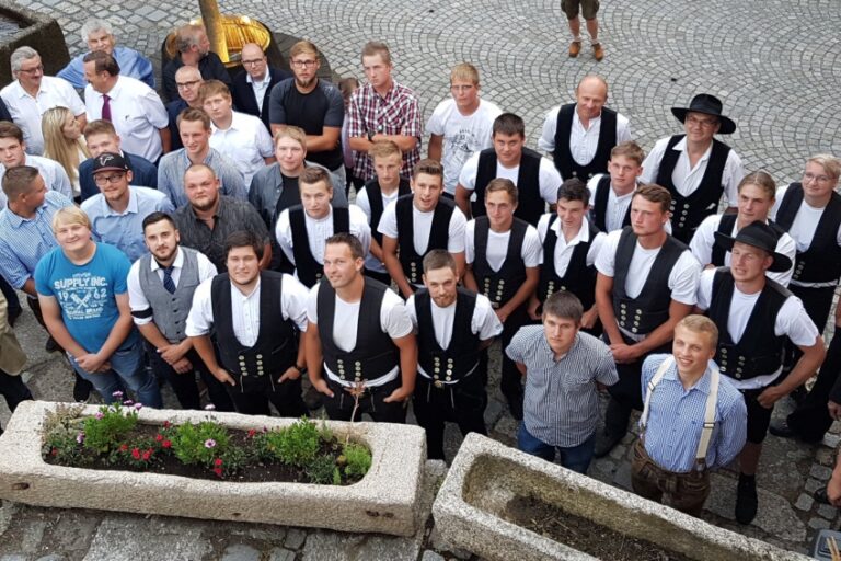 Große Gruppe junger Handwerker in traditioneller Zimmermannskleidung und zivil gekleideten Personen, Aufnahme von oben.