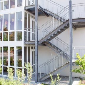 Außentreppe aus Metall mit Geländer an einem modernen Gebäude mit großer Fensterfront.