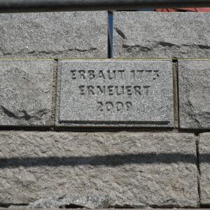 Nahaufnahme einer Steinplatte in einer Mauer mit Gravur: „Erbaut 1777, Erneuert 2009“.