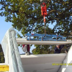 Kran hebt ein vorgefertigtes Betonelement für die Decke in Position, zwei Arbeiter richten das Bauteil ein.