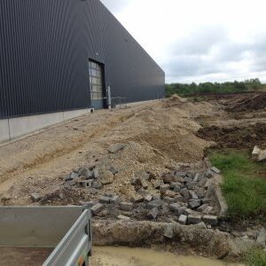 Baustelle neben einer Industriehalle mit aufgerissener Pflasterung und Erdanhäufungen.