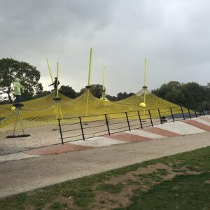 Kinder spielen in Regenjacken auf einem großen Netzspielplatz mit gelben Netzen und rot-weißer Rampe.