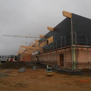 Neubau mit Ziegelmauerwerk im Baufortschritt, darüber werden Dachträger aus Holz montiert.