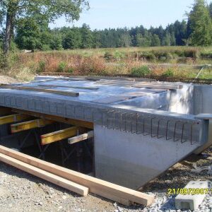 Neubau eines Brückendurchlasses mit Betonfertigteilen und Stützkonstruktion in ländlicher Umgebung.