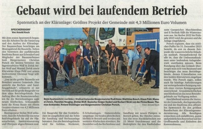 Zeitungsausschnitt mit der Überschrift „Gebaut wird bei laufendem Betrieb“ zeigt eine Gruppe von Männern mit Spaten auf einer Baustelle vor einem Bagger.