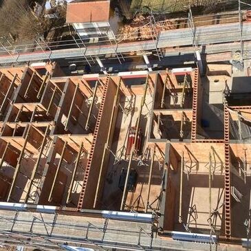 Blick von oben auf eine Baustelle eines mehrgeschossigen Gebäudes mit bereits errichteten Innenwänden und Gerüsten.