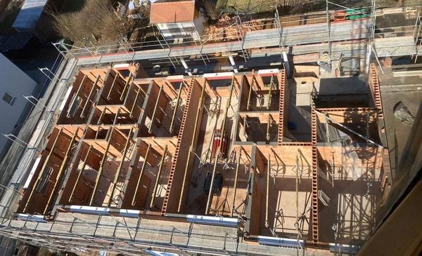 Blick von oben auf eine Baustelle eines mehrgeschossigen Gebäudes mit bereits errichteten Innenwänden und Gerüsten.