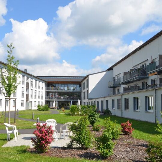 Modernes Pflegeheim oder Wohnkomplex mit Gartenanlage, Wegen, Blumenbeeten und Sitzgelegenheiten im Innenhof.