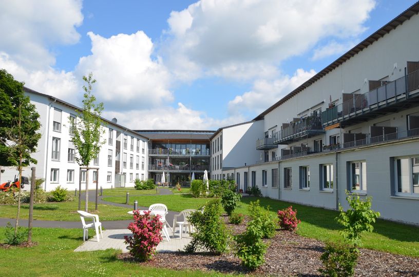 Modernes Pflegeheim oder Wohnkomplex mit Gartenanlage, Wegen, Blumenbeeten und Sitzgelegenheiten im Innenhof.