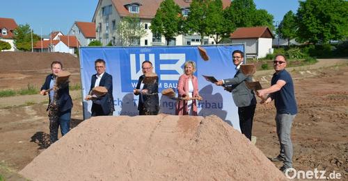 Sechs Personen werfen gemeinsam Sand in die Luft. Im Hintergrund ein Werbebanner der Firma WEB und Wohngebäude mit rotem Dach.
