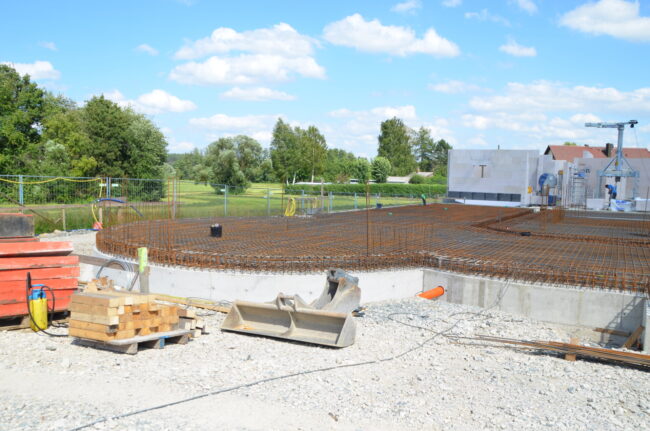 Mitarbeiter einer Baufirma mit Warnwesten posieren gemeinsam auf einer Baustelle mit Kran im Hintergrund.