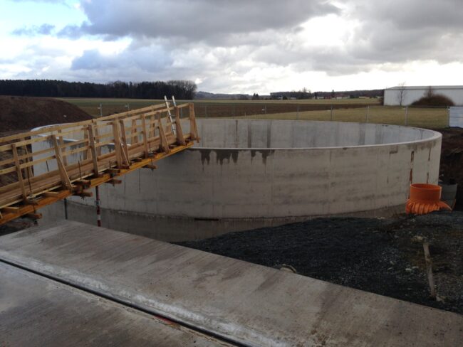 Gebäude mit Klinkerfassade und moderner Architektur, umgeben von bepflanzten Grünflächen und Wegen.