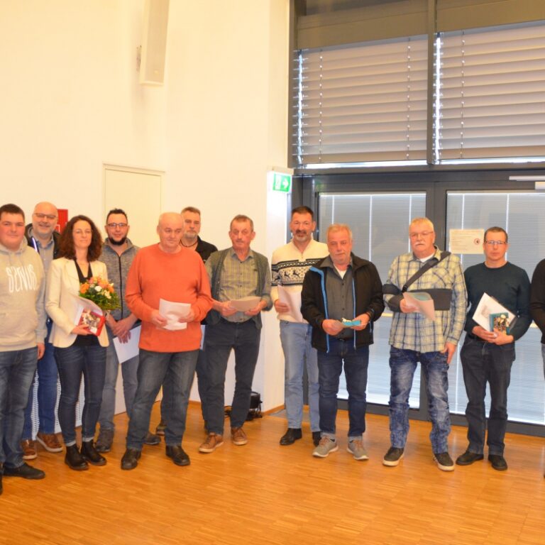 Eine Gruppe von etwa 15 Personen posiert in einem Innenraum mit Urkunden, eine Frau hält einen Blumenstrauß.